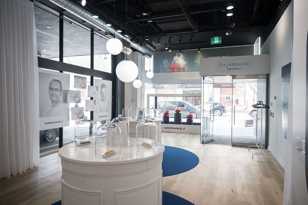 Interior of La p&acirc;tisserie pop-up showing glass cloches with pastries, chef portraits, and pendant globe lighting