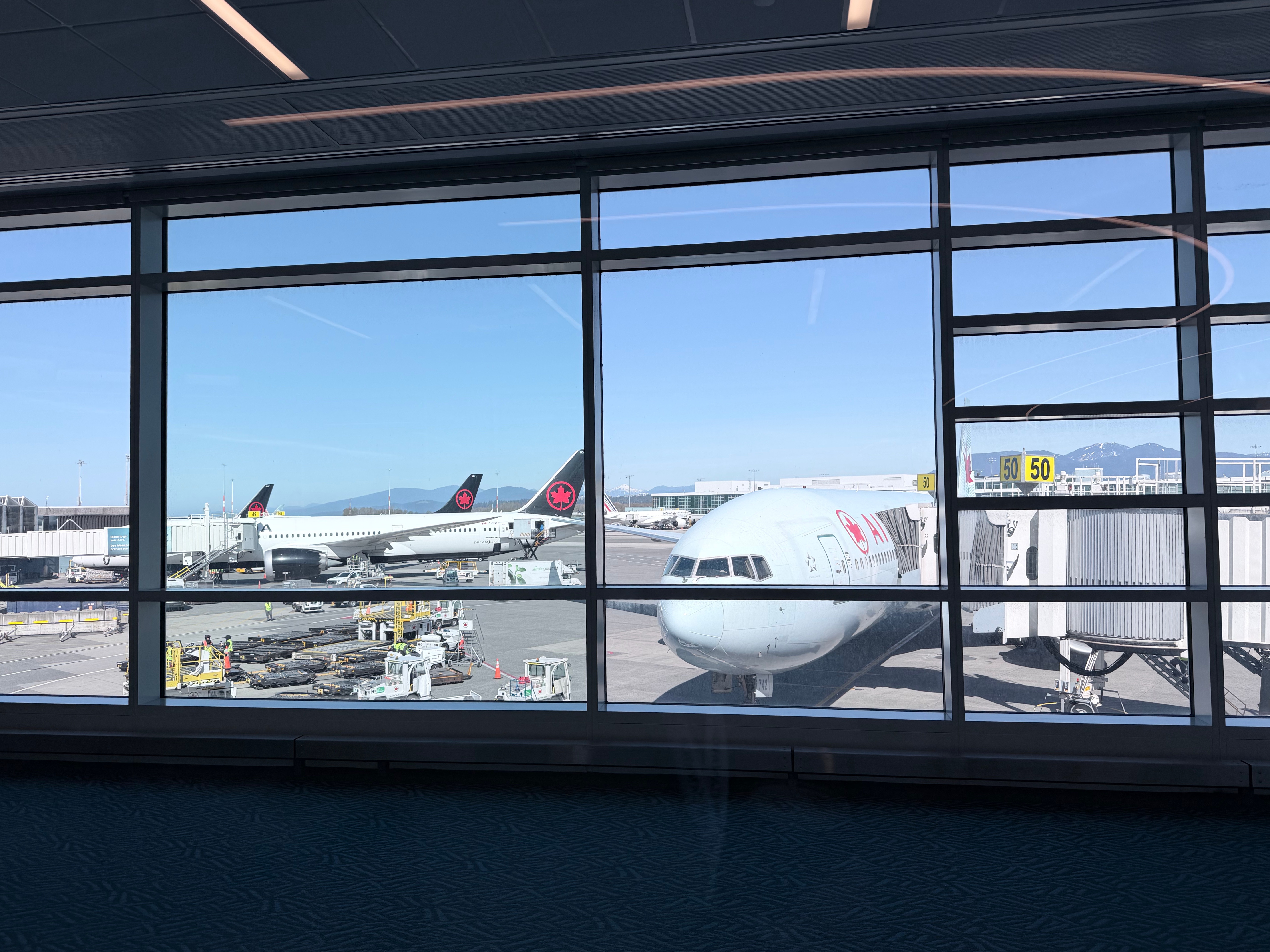 View through full-height windows at the Air Canada Café YVR showing Air Canada aircraft on the tarmac and mountains