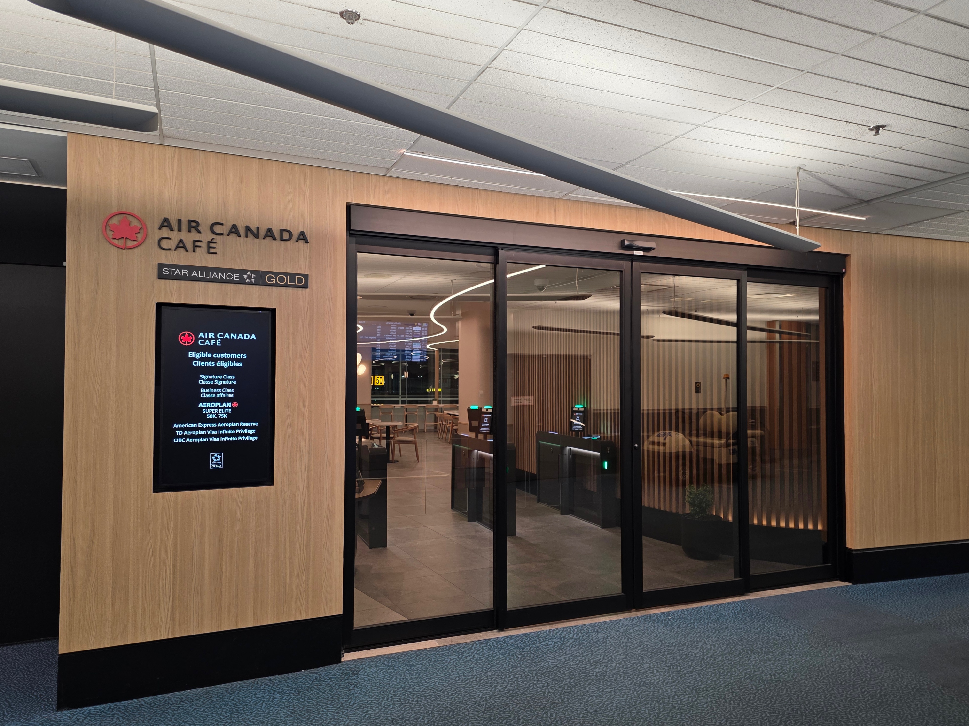 Entrance to the Air Canada Café at YVR Gate C50 with sliding glass doors and digital eligibility sign
