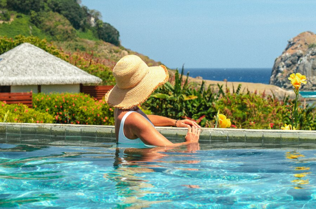 Woman in a sun hat relaxing in an infinity pool overlooking the ocean during a Preferred Hotels stay