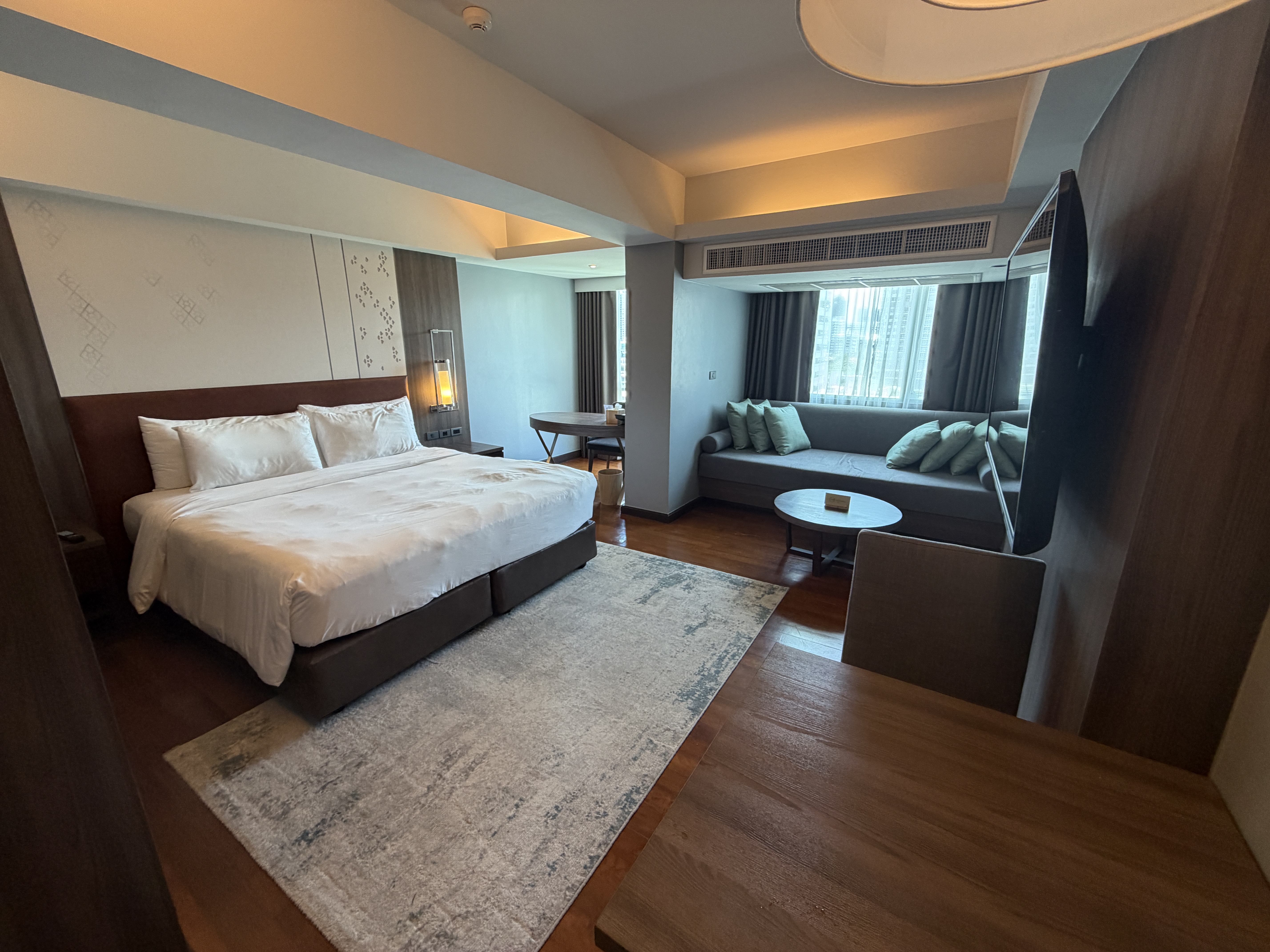 King bedroom with lounge seating area and cityscape windows at Novotel Living Bangkok Sukhumvit Legacy