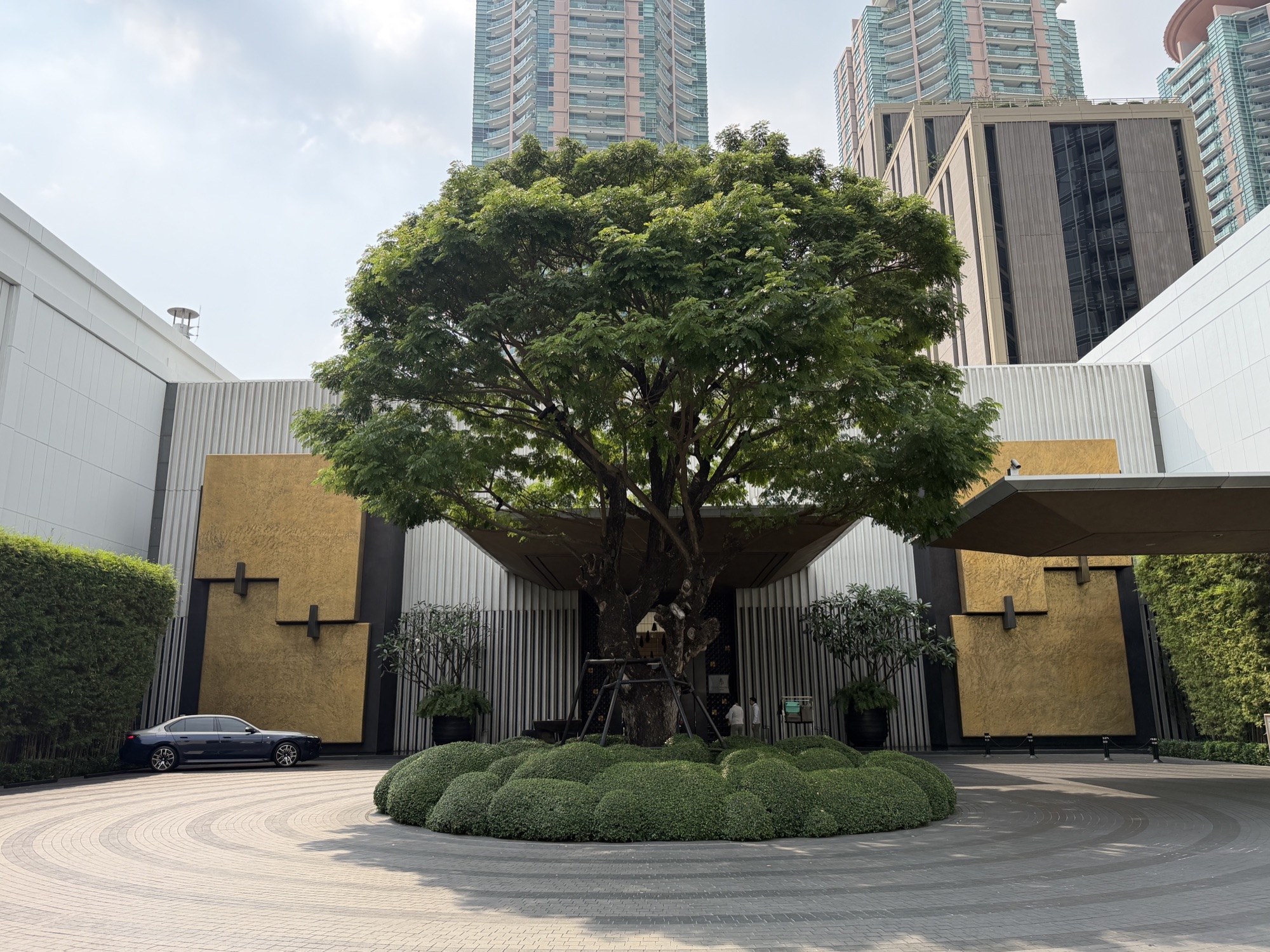 Arrival courtyard with a mature rain tree and gold-leaf panels at the entrance of Four Seasons Hotel Bangkok at Chao Phraya River