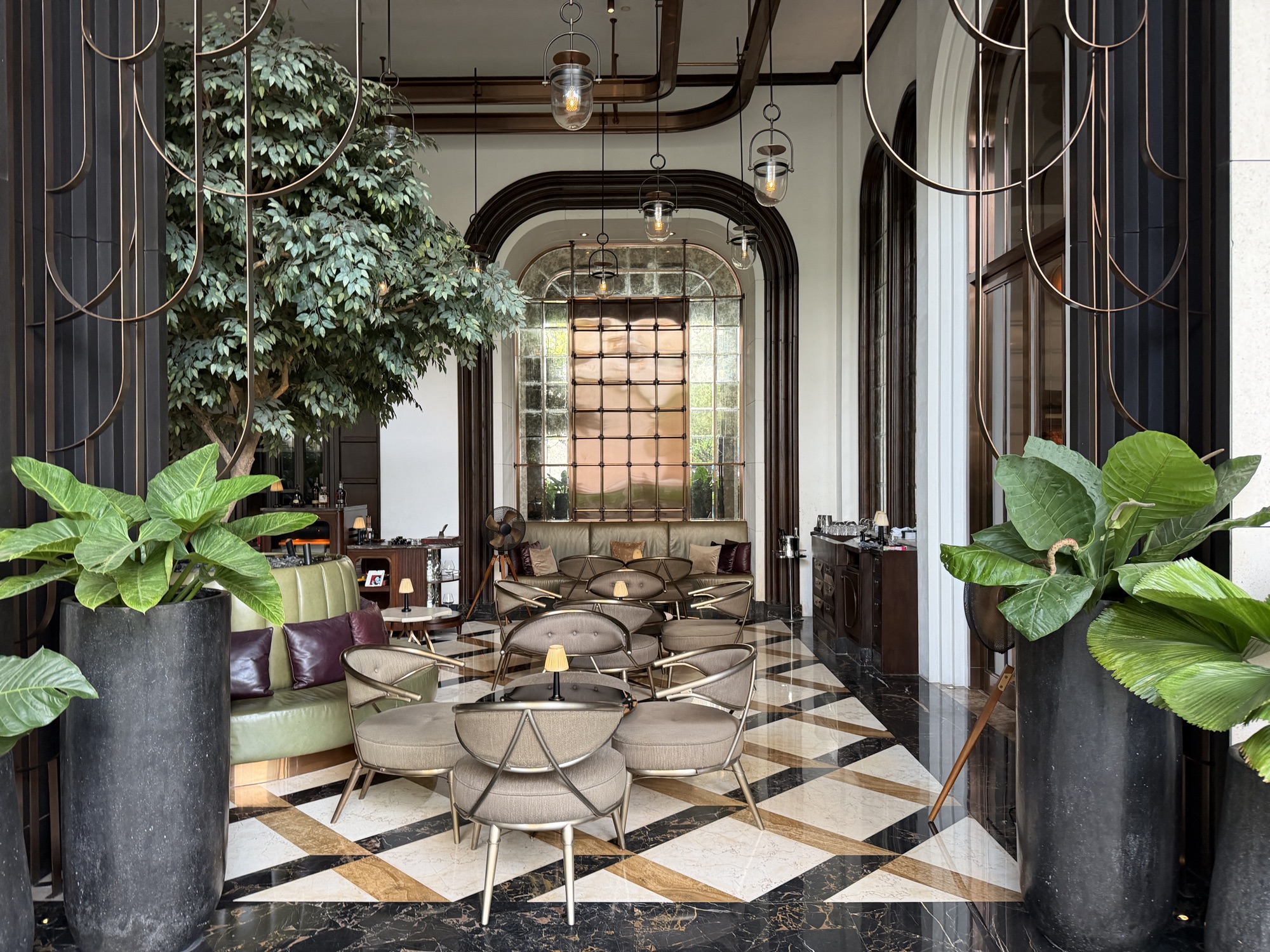 Art Deco lounge of BKK Social Club with green leather banquettes, brass screens, and a chevron marble floor at Four Seasons Hotel Bangkok at Chao Phraya River
