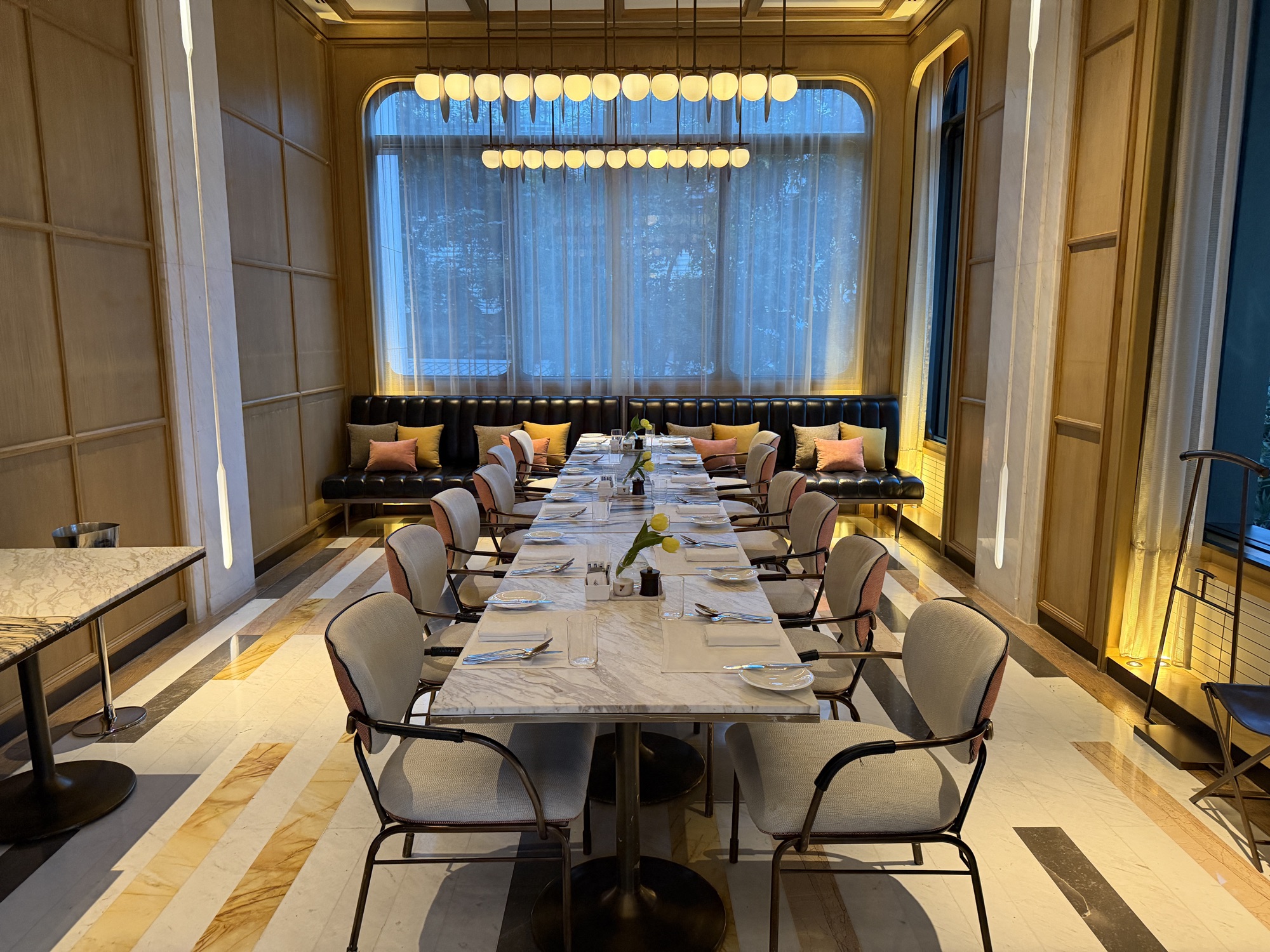 A communal table sits beneath a run of pendant lights. at Four Seasons Hotel Bangkok at Chao Phraya River