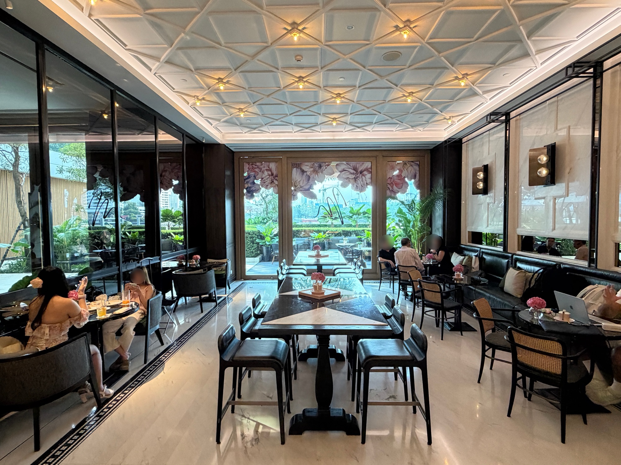 Café Madeleine interior with coffered ceiling, marble tables, and floral windows at Four Seasons Hotel Bangkok at Chao Phraya River