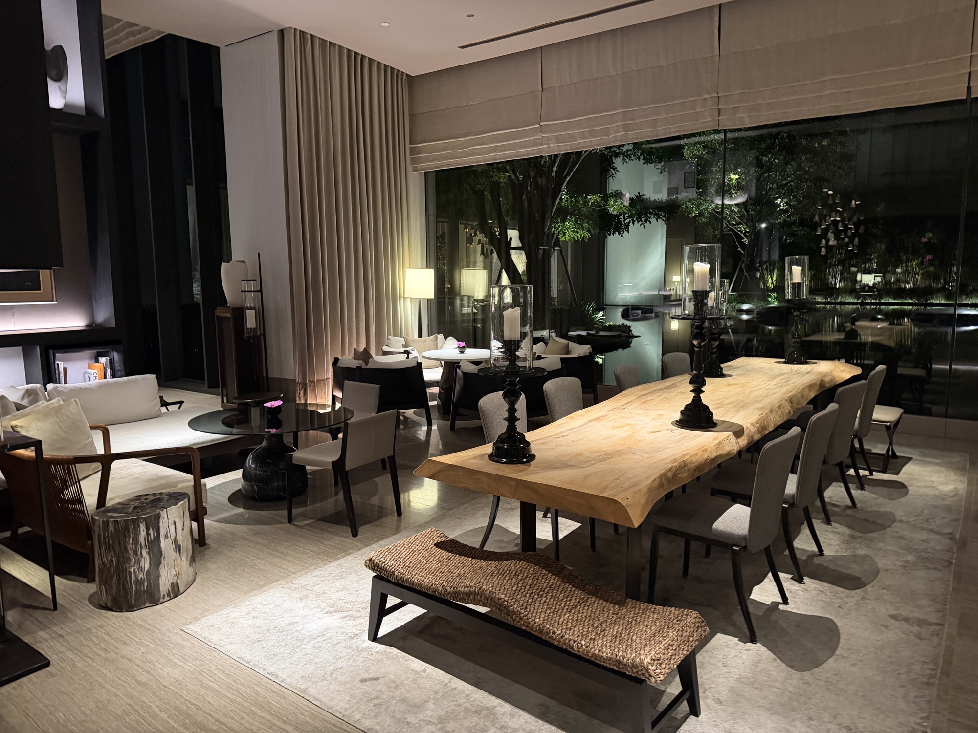Lobby lounge with a communal live-edge table and garden views at night at Four Seasons Hotel Bangkok at Chao Phraya River