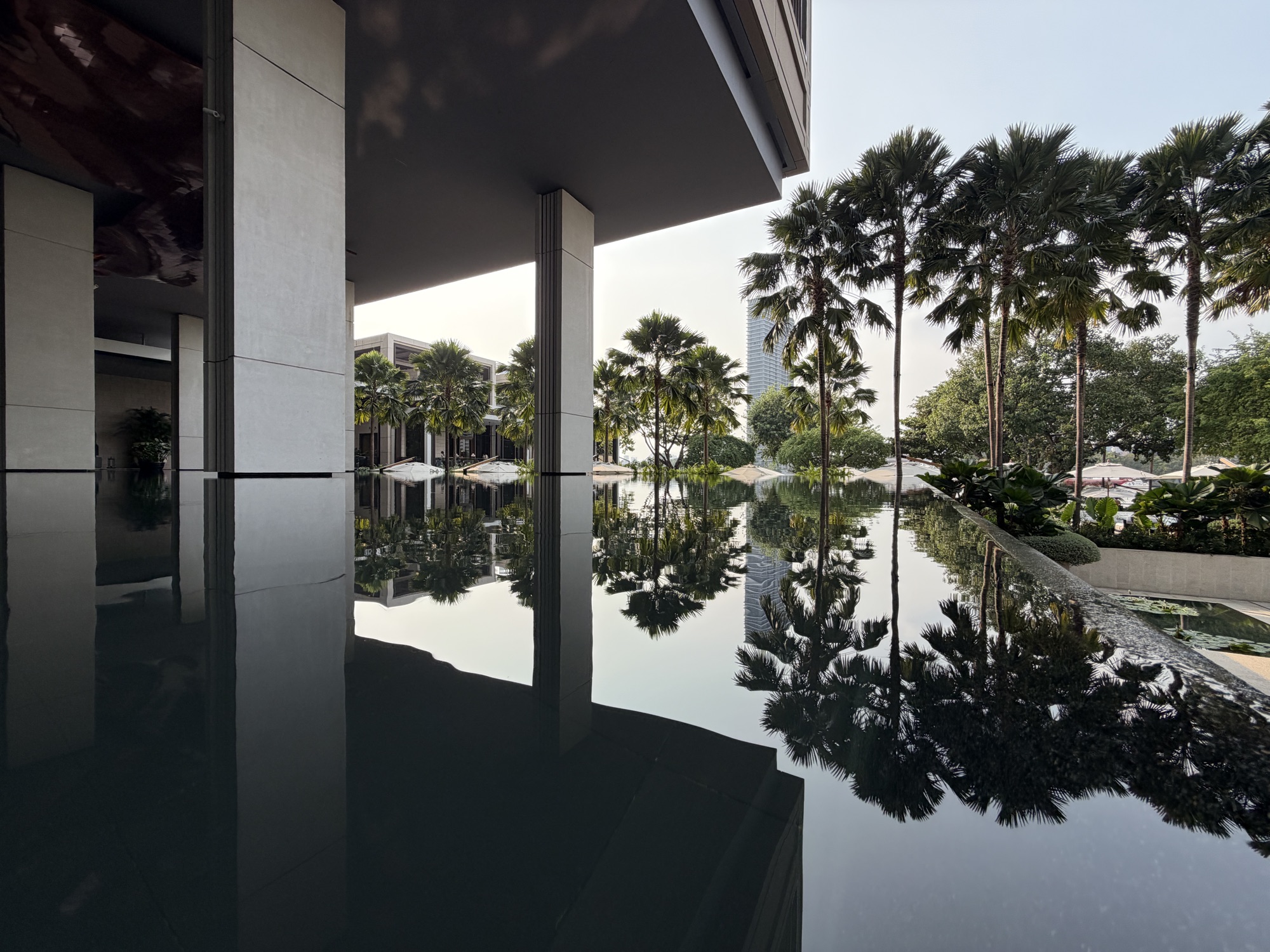 Mirror-still ornamental water feature reflecting palm trees in a covered walkway at Four Seasons Hotel Bangkok at Chao Phraya River