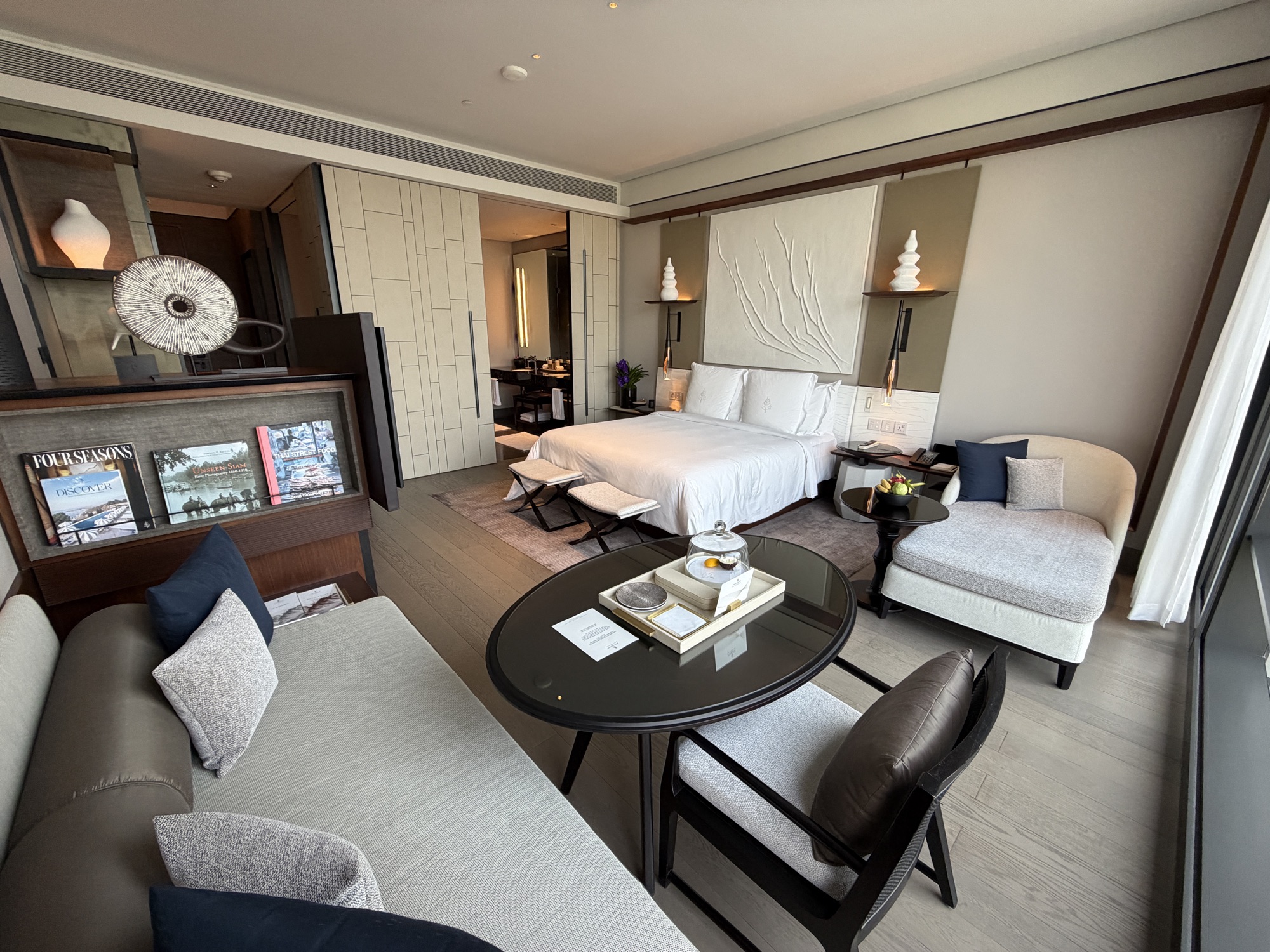 Wide view of the Deluxe River-View Room with sitting area, dining table, and king bed at Four Seasons Hotel Bangkok at Chao Phraya River