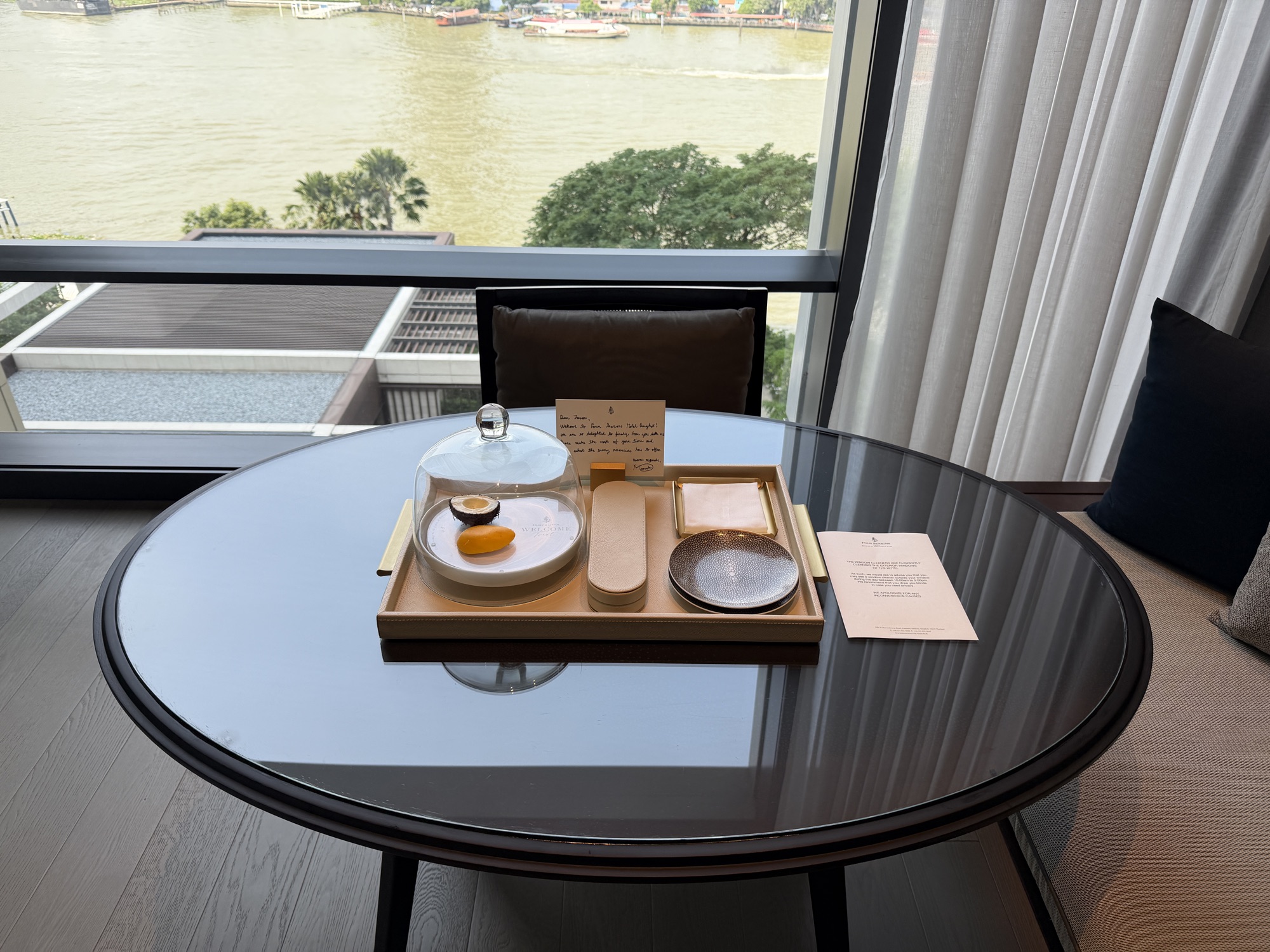 Round table with welcome amenity by the window in the Deluxe River-View Room at Four Seasons Hotel Bangkok at Chao Phraya River