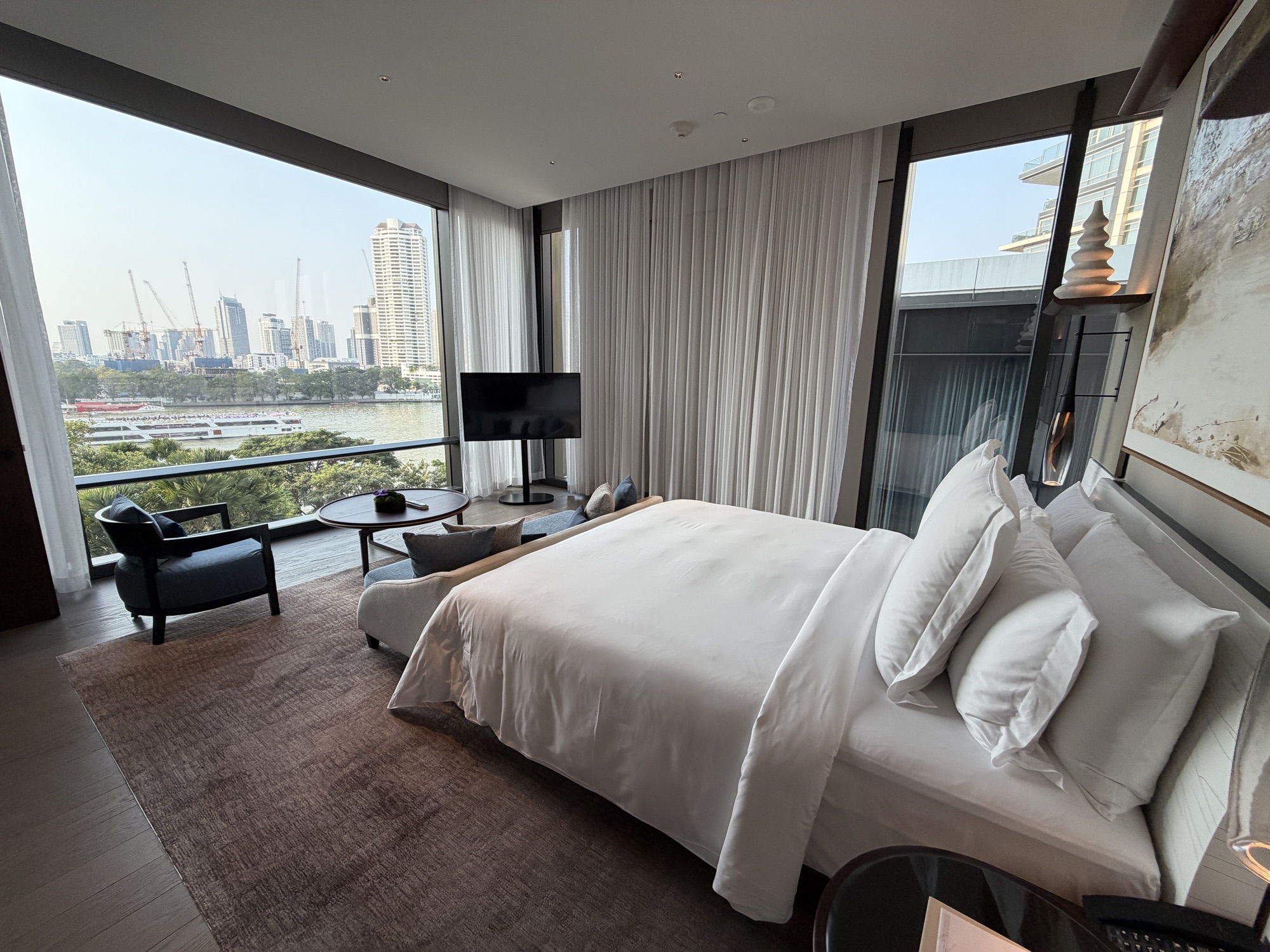 Executive Suite bedroom with river views and a reading chair at Four Seasons Hotel Bangkok at Chao Phraya River