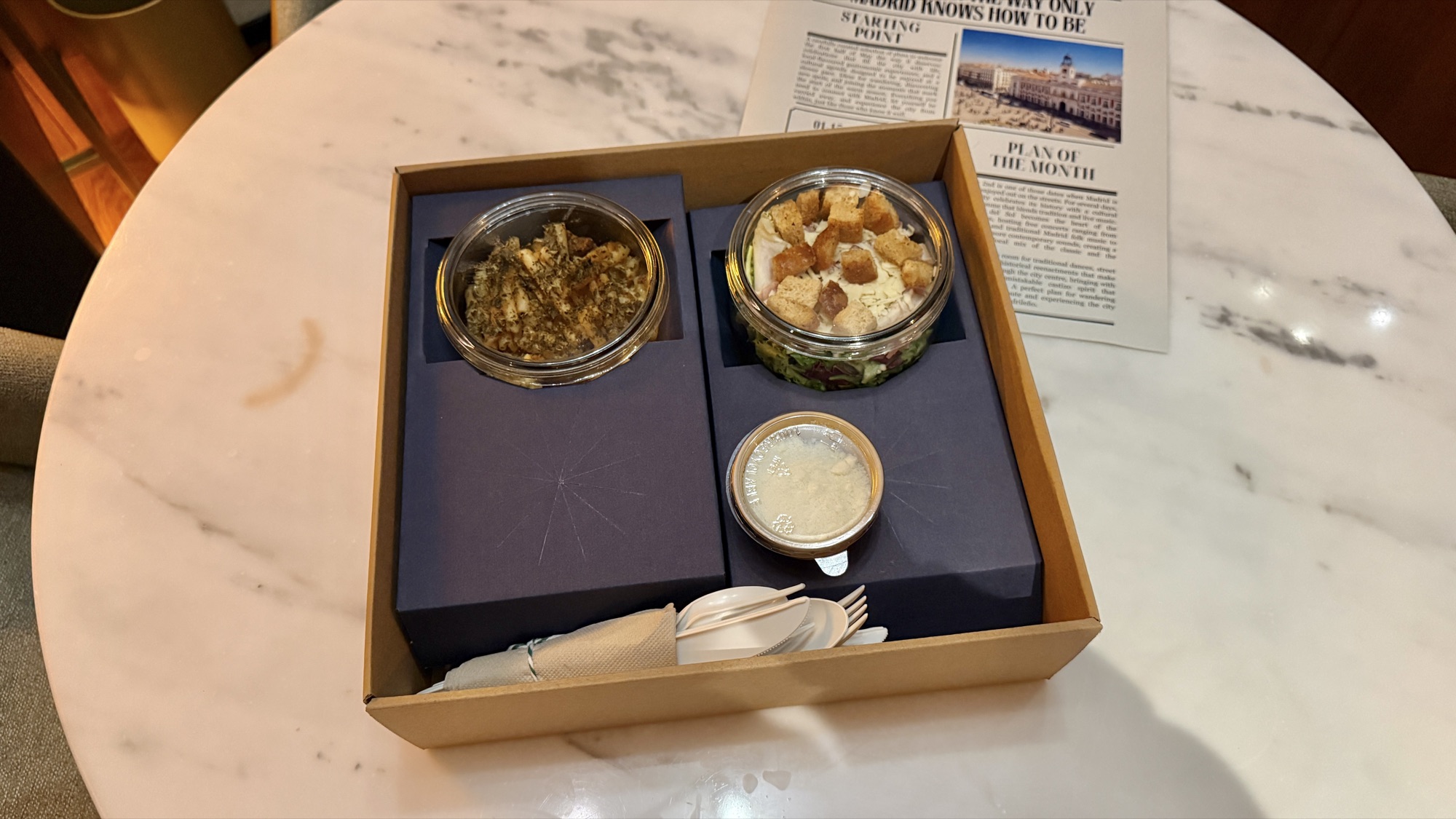 In-room dining delivered in glass jars inside a kraft box beside the hotel newsletter