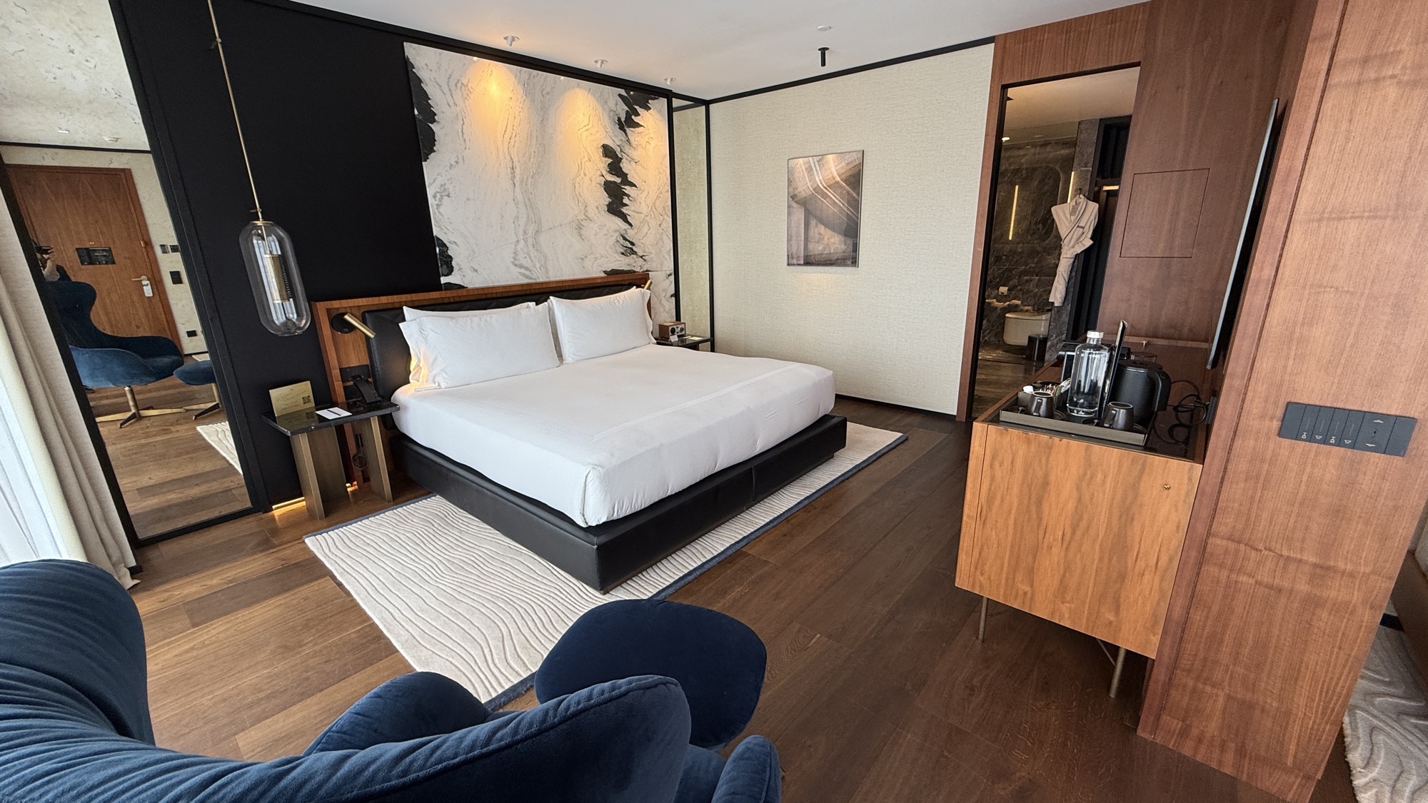Junior Suite bedroom with a marble wall, blue armchairs, and minibar