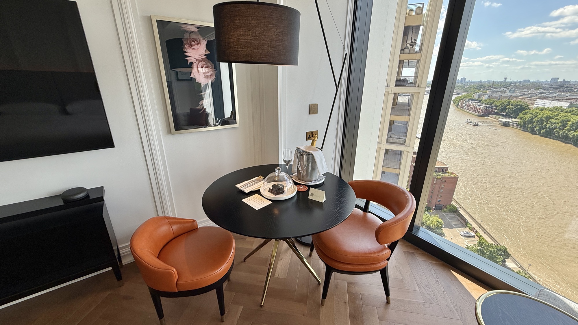 Round dining table with two tan leather chairs by the window, a framed artwork, and a river view