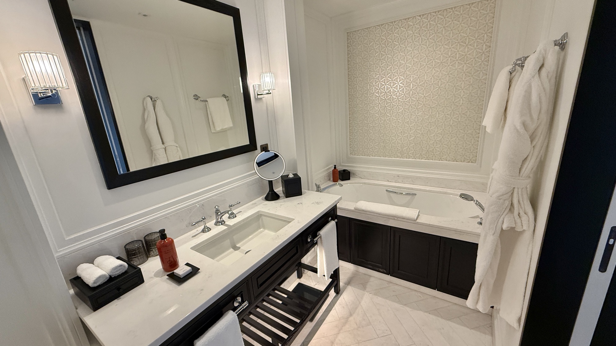 Bathroom vanity and deep bathtub with a robe hanging beside the mirror