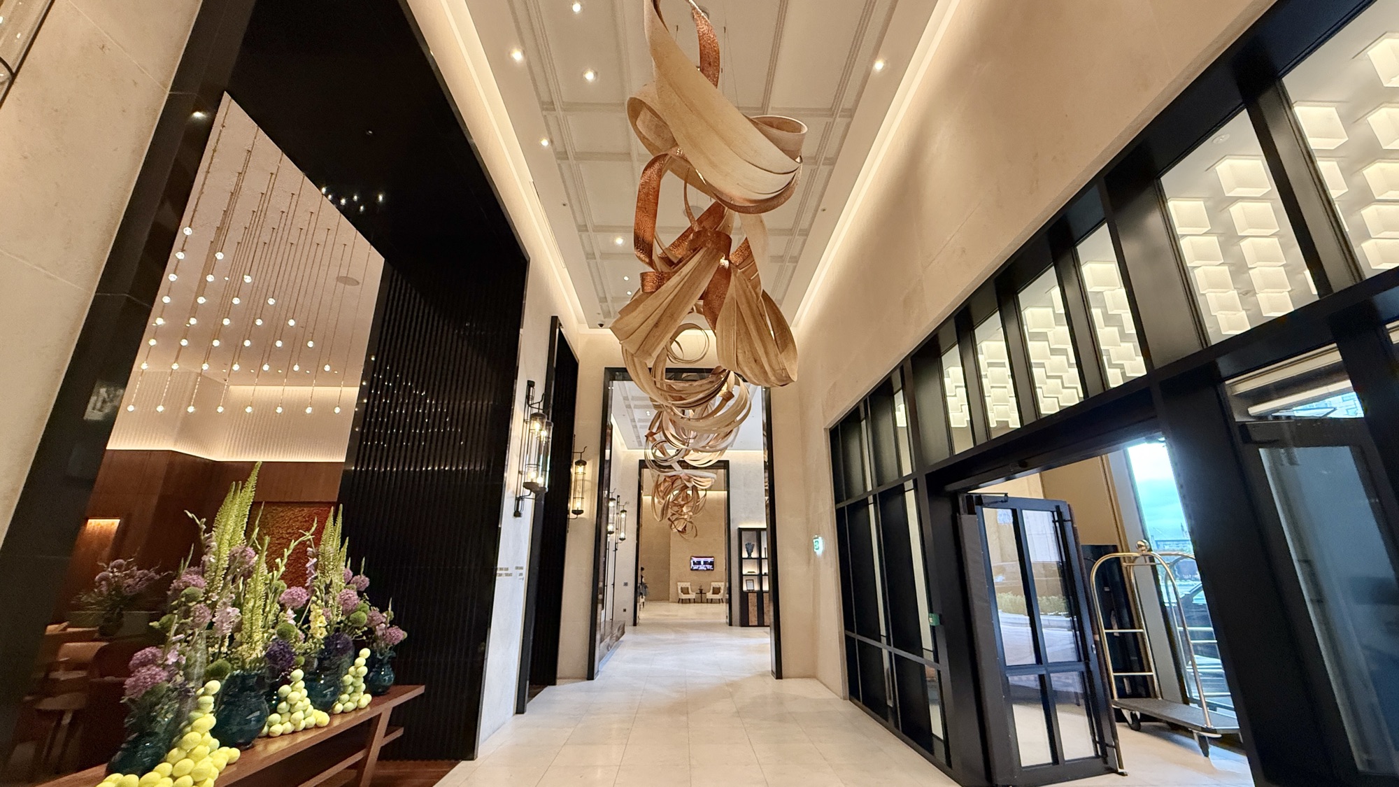 Lobby corridor at Park Hyatt London River Thames with the copper ribbon sculpture overhead and a floral arrangement