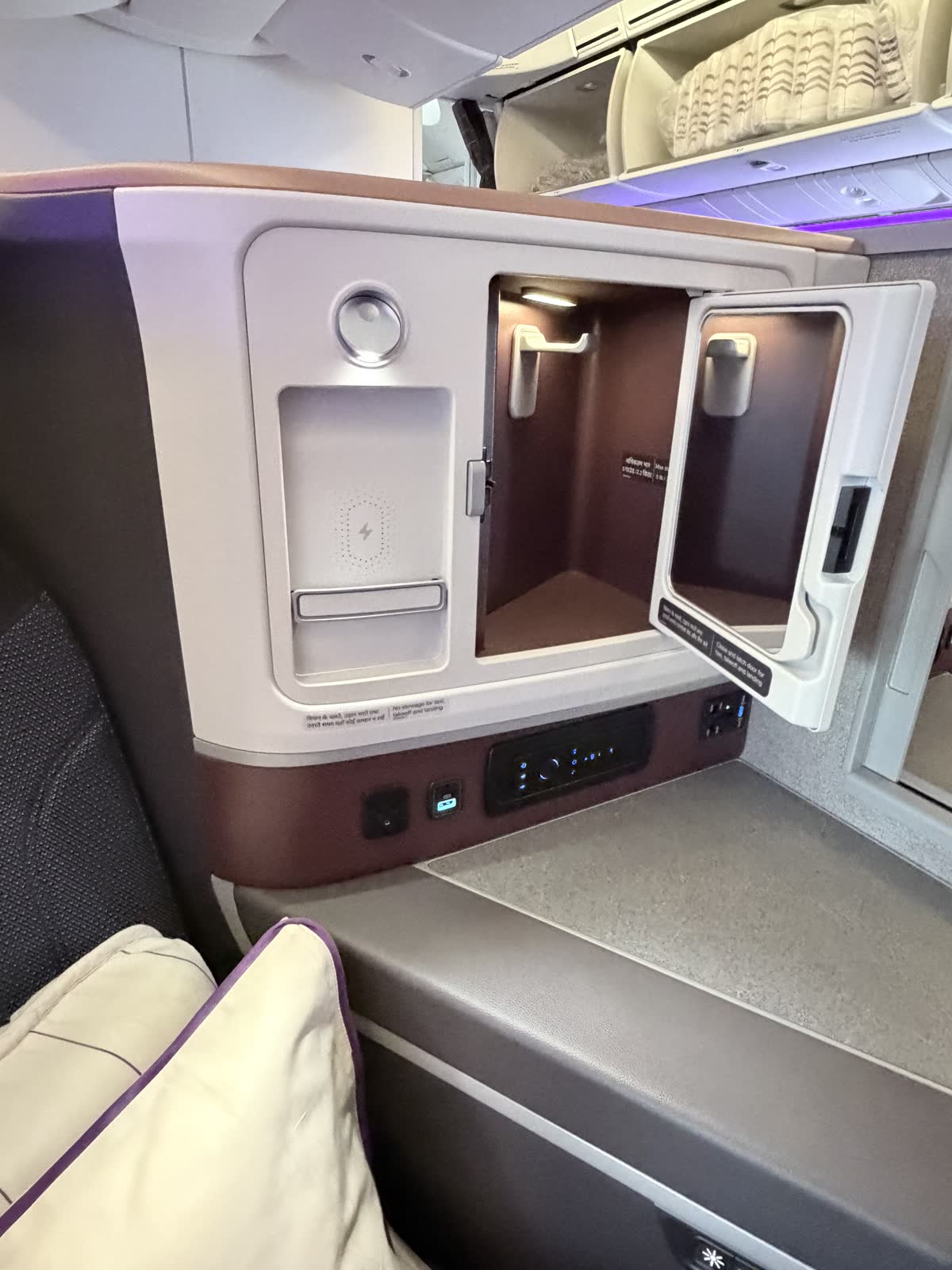 Business class side cubby with its door open beside an upright wireless charging slot, a control panel, and charging ports