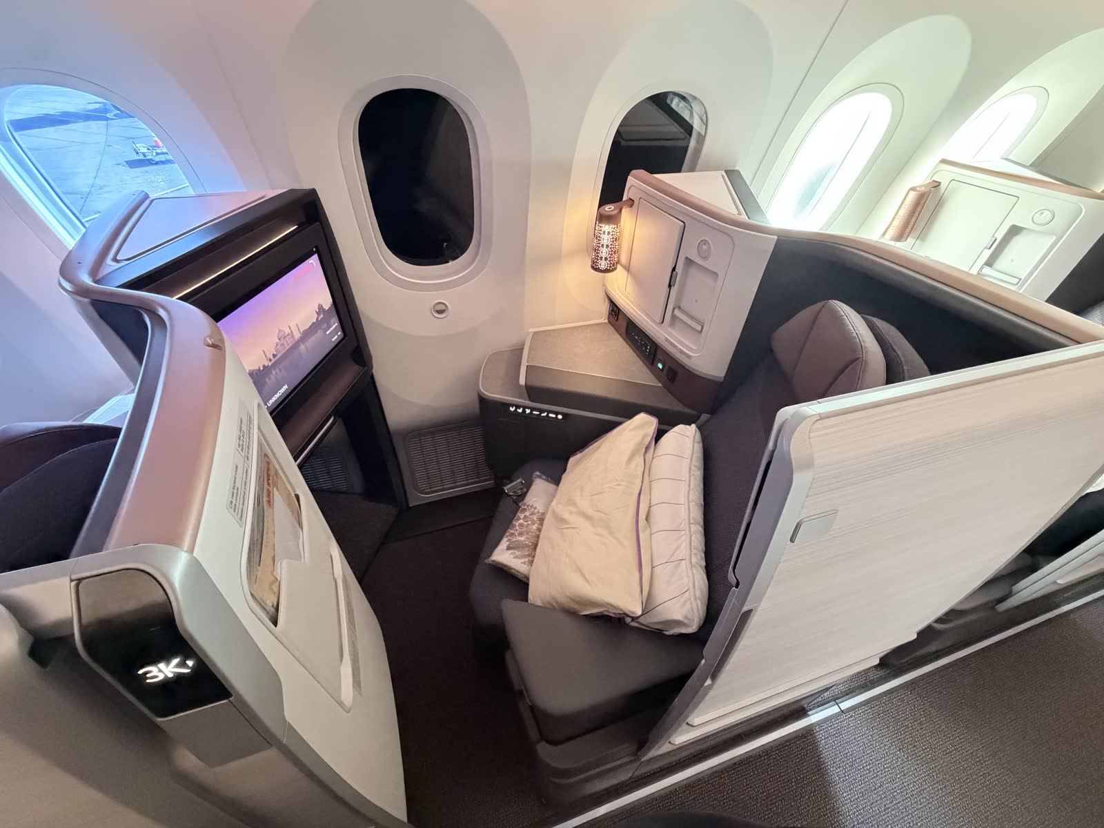 Air India 787-9 business class window suite 3K with pillows, a side console, a lit feature lamp, and a seatback screen