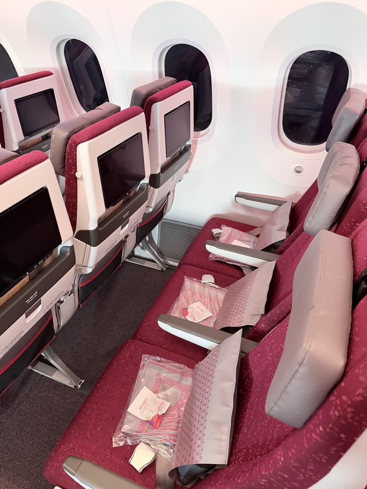 Economy seats with a pillow and a packaged blanket on each, facing the seatback screens of the row ahead