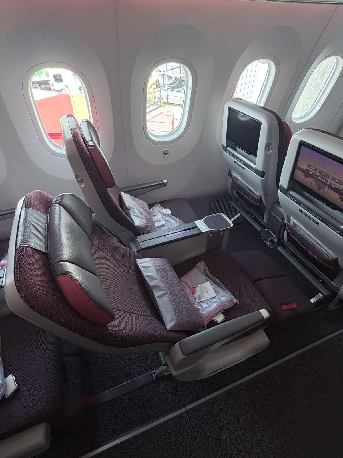 Two premium economy seats by the window, the nearer one reclined with its calf rest raised and the window seat upright