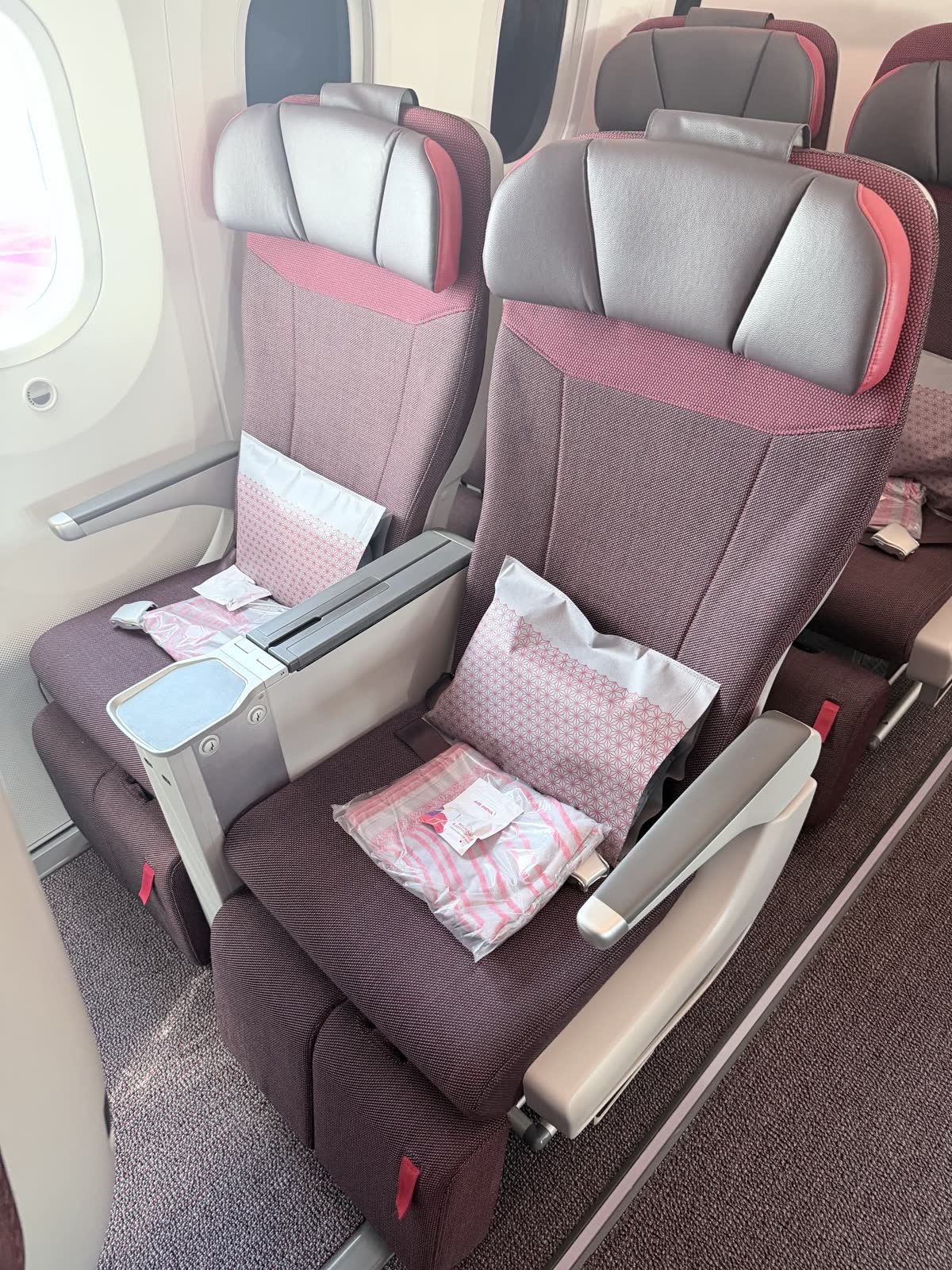 Two premium economy seats by the window, with a pillow and a packaged blanket on each