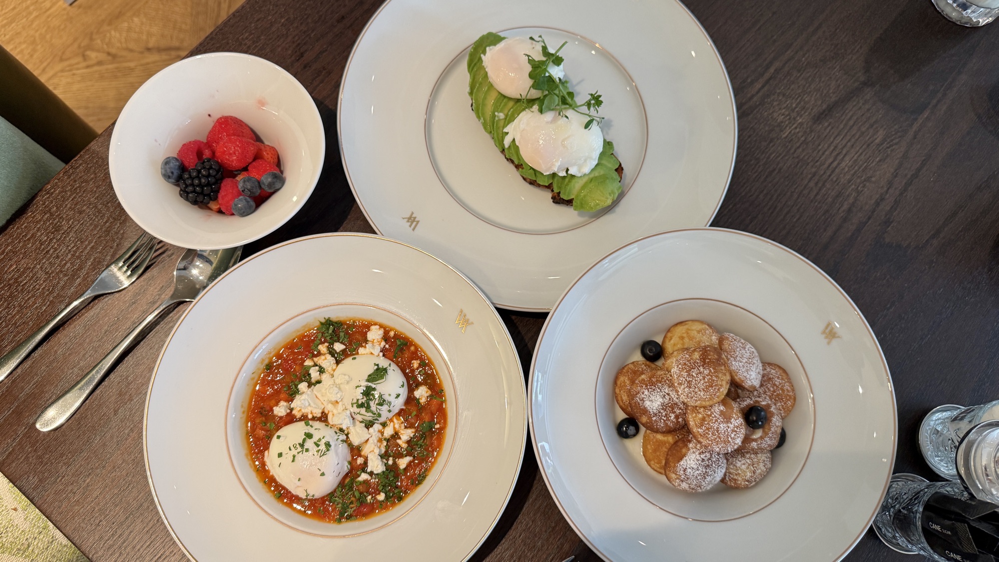 Breakfast plates of poached eggs on avocado, shakshuka, Dutch mini pancakes, and fresh berries