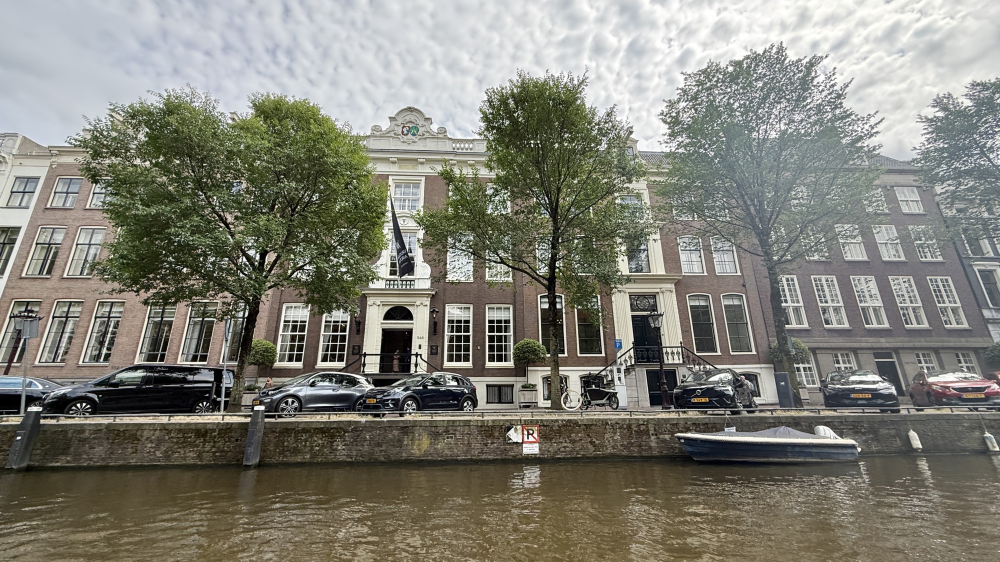 The Waldorf Astoria Amsterdam's canal-house facades seen across the Herengracht, with trees and moored boats