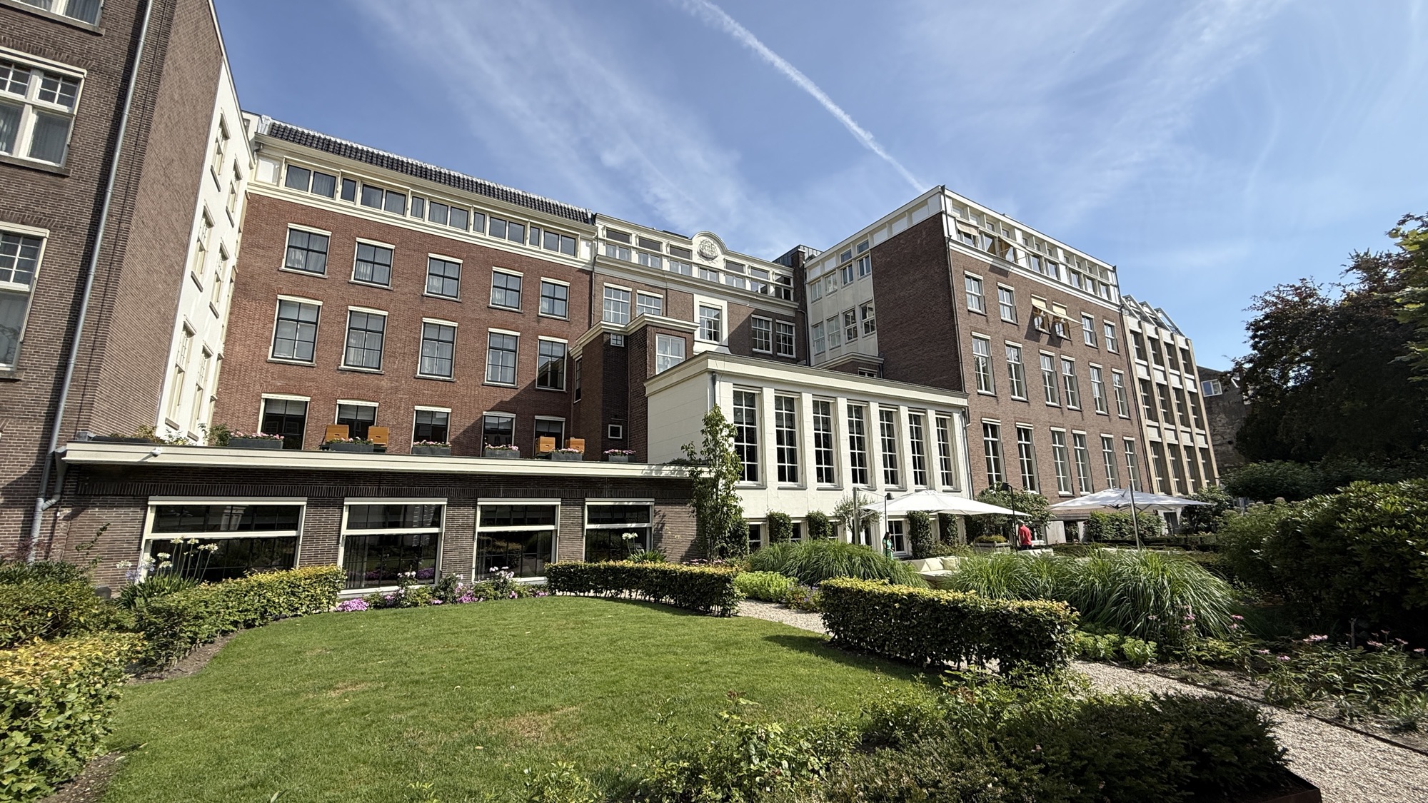 View of the Waldorf Astoria Amsterdam's brick facade from the private garden lawn