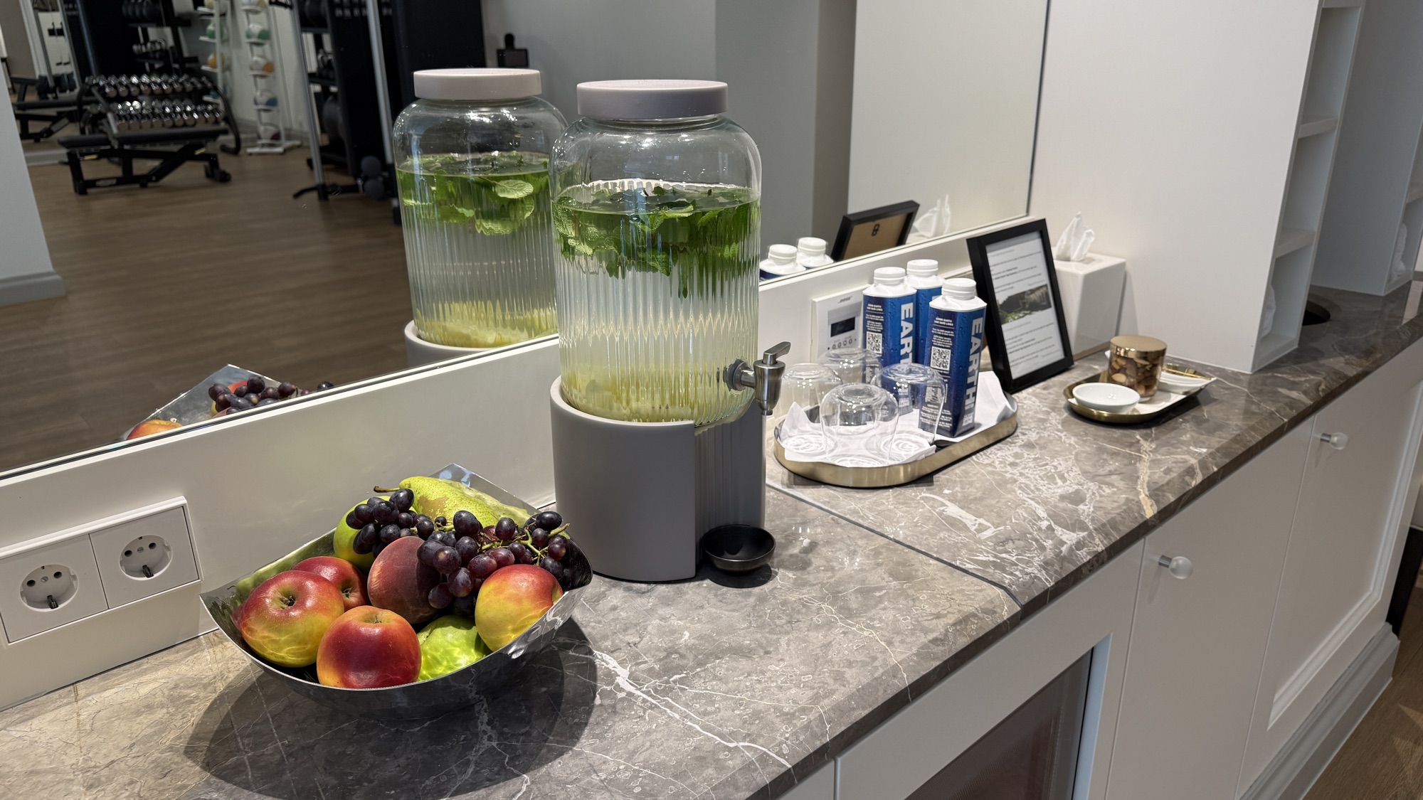 Infused water, fruit, and snacks laid out on a marble counter beside the fitness centre