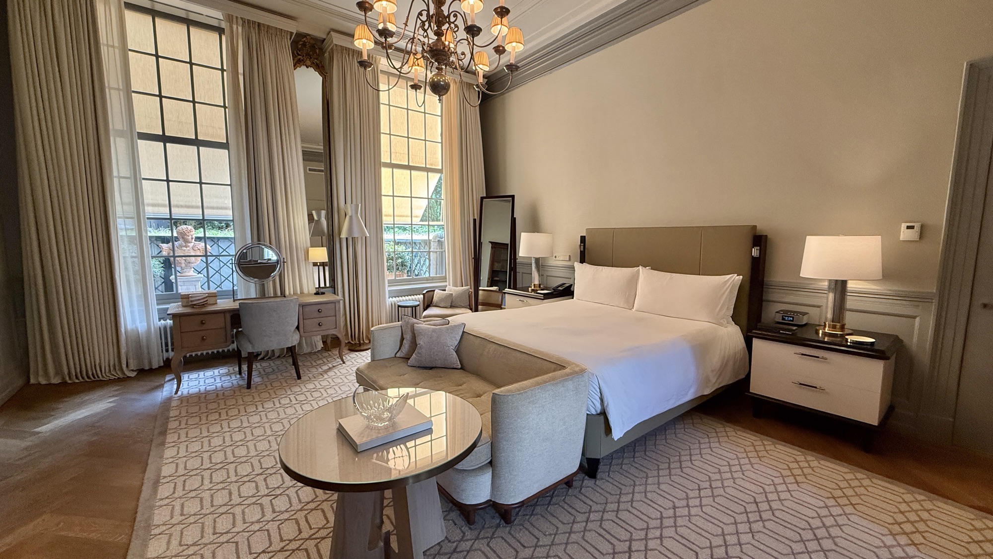 Bedroom of the Van Loon Suite with high ceilings, a chandelier, and tall windows